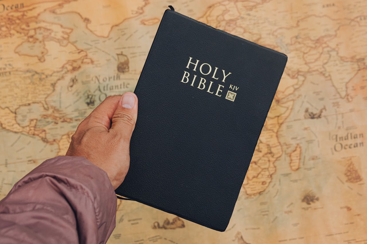 Close-up of a hand holding a Holy Bible above a vintage world map.