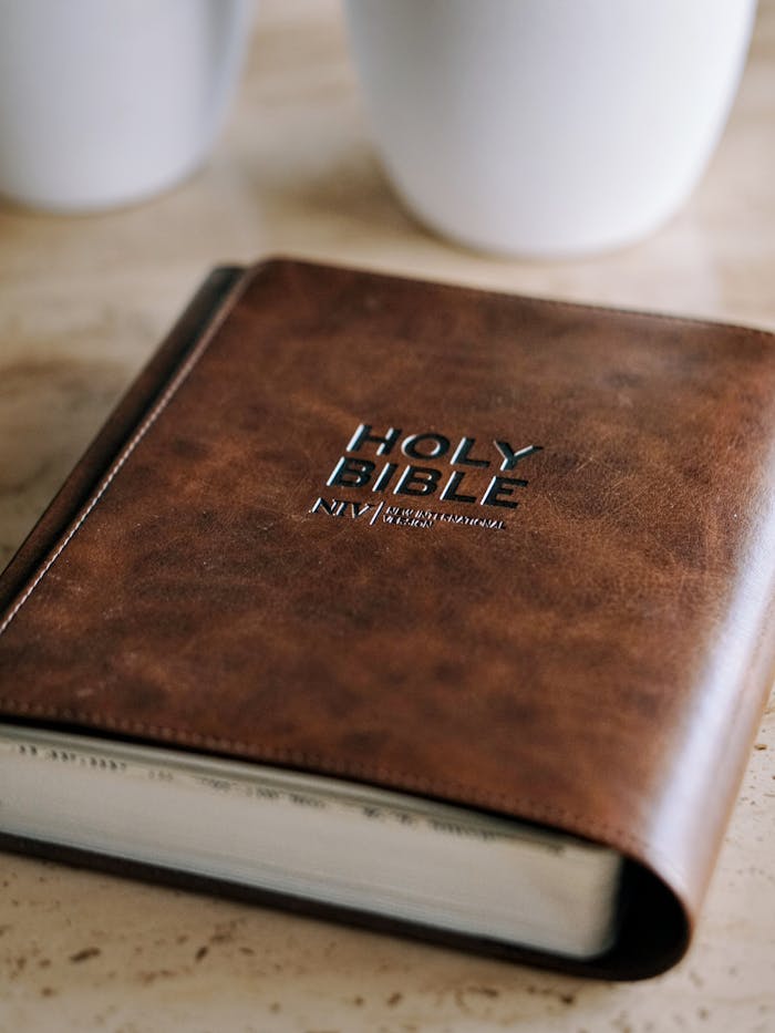 Brown leather-bound Holy Bible on a wooden table with two white mugs in the background.