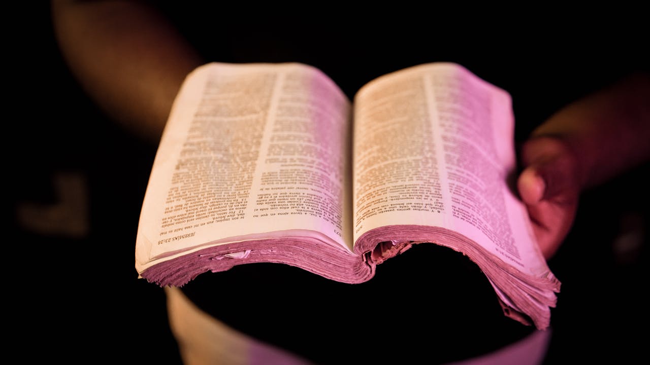 An open Bible held in hands with dramatic lighting, creating a serene atmosphere.